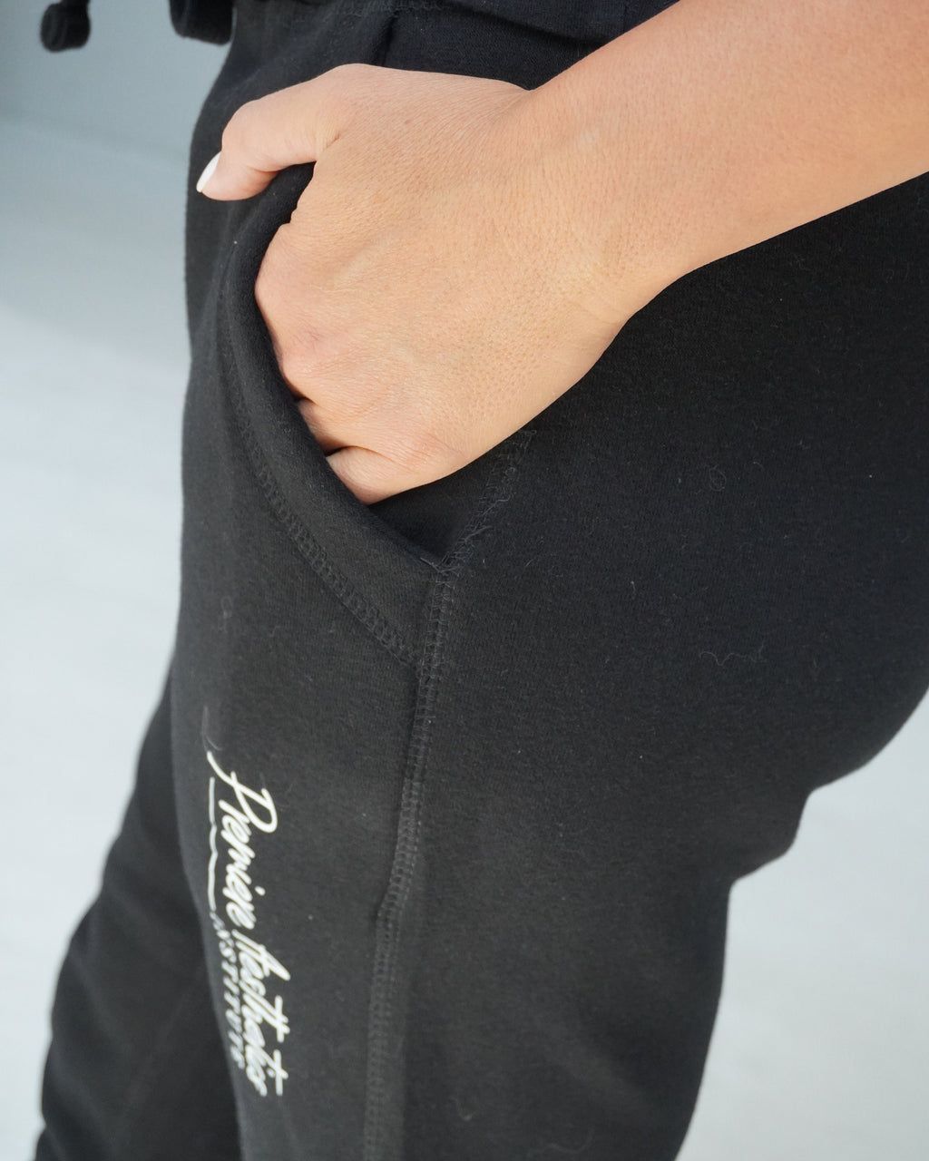 Close-up of a person wearing black sweatpants with a side pocket, hand in pocket, and white script text near the lower leg.